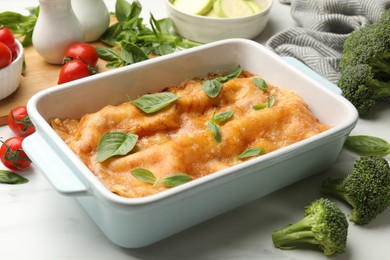 Photo of Tasty vegetarian lasagna in baking dish and ingredients on white table, closeup