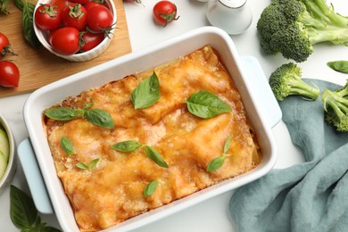 Photo of Tasty vegetarian lasagna in baking dish and ingredients on white table, flat lay