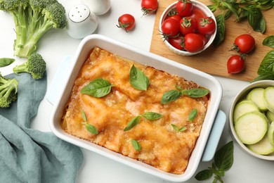 Photo of Tasty vegetarian lasagna in baking dish and ingredients on white table, flat lay
