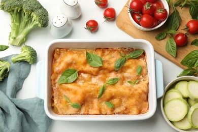 Photo of Tasty vegetarian lasagna in baking dish and ingredients on white table, flat lay