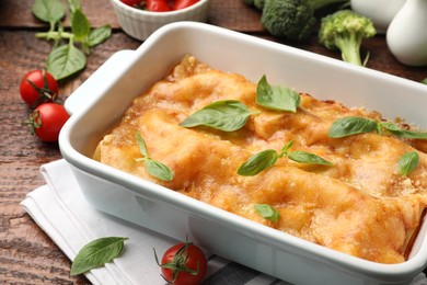 Photo of Tasty vegetarian lasagna in baking dish and ingredients on wooden table, closeup