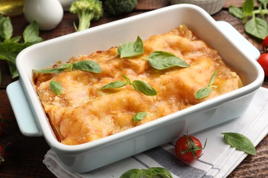 Photo of Tasty vegetarian lasagna in baking dish and ingredients on wooden table, closeup