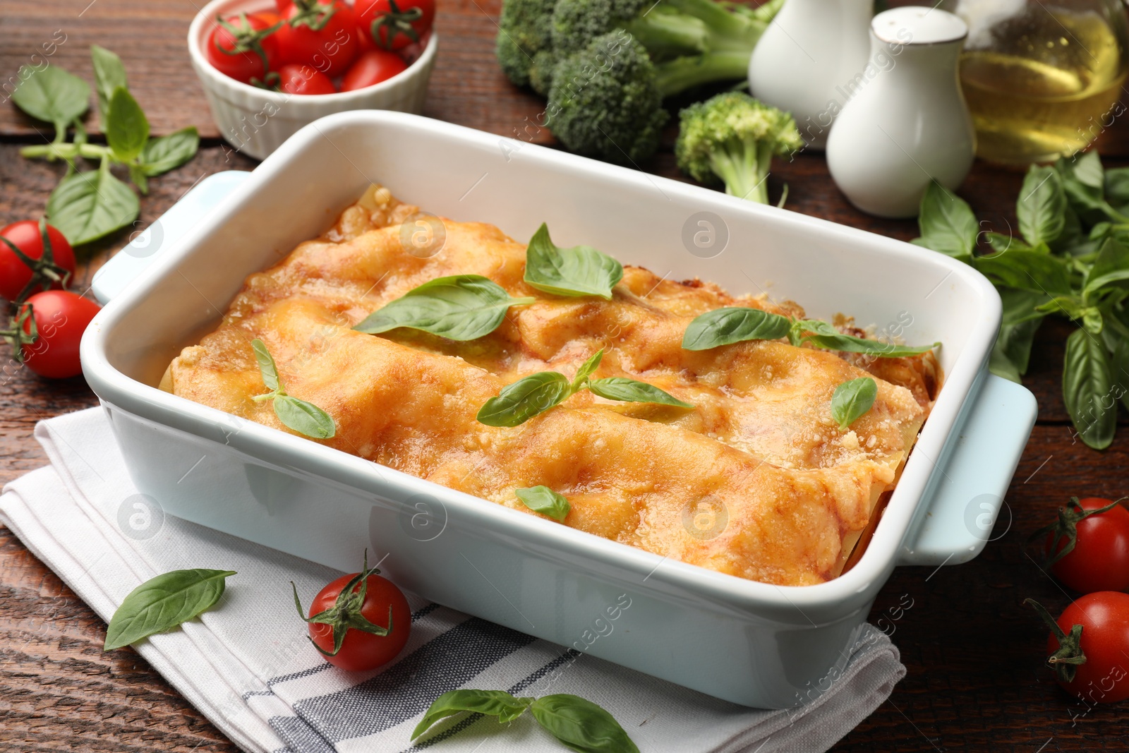 Photo of Tasty vegetarian lasagna in baking dish and ingredients on wooden table, closeup