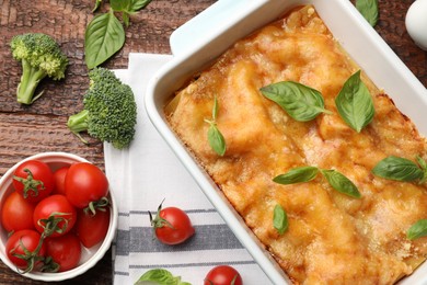 Photo of Tasty vegetarian lasagna in baking dish and ingredients on wooden table, flat lay
