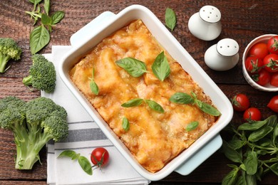 Photo of Tasty vegetarian lasagna in baking dish and ingredients on wooden table, flat lay