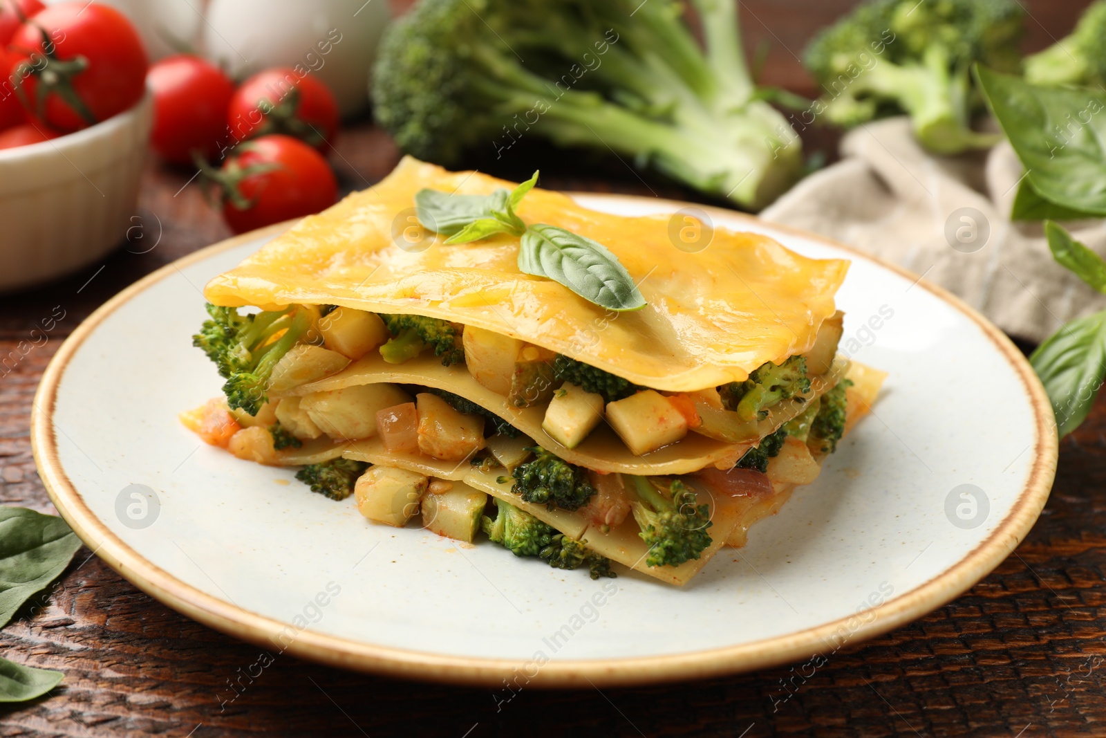Photo of Piece of tasty vegetarian lasagna and ingredients on wooden table, closeup