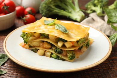 Photo of Piece of tasty vegetarian lasagna and ingredients on wooden table, closeup