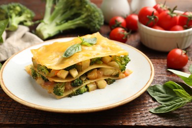 Photo of Piece of tasty vegetarian lasagna and ingredients on wooden table, closeup