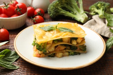 Photo of Piece of tasty vegetarian lasagna and ingredients on wooden table, closeup