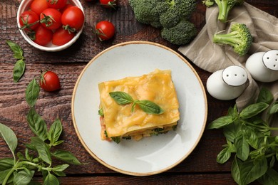 Photo of Piece of tasty vegetarian lasagna and ingredients on wooden table, flat lay