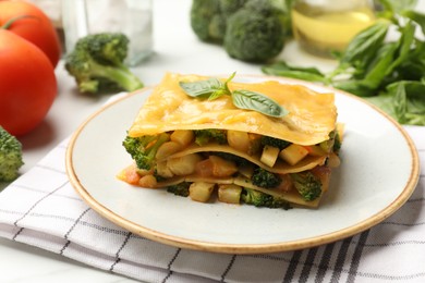 Photo of Piece of tasty vegetarian lasagna and ingredients on white table, closeup