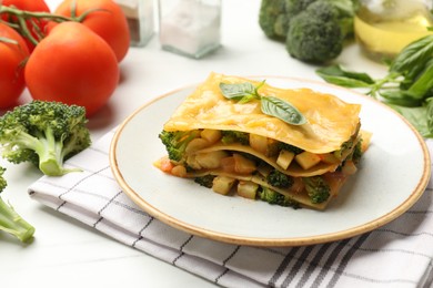 Photo of Piece of tasty vegetarian lasagna and ingredients on white table, closeup