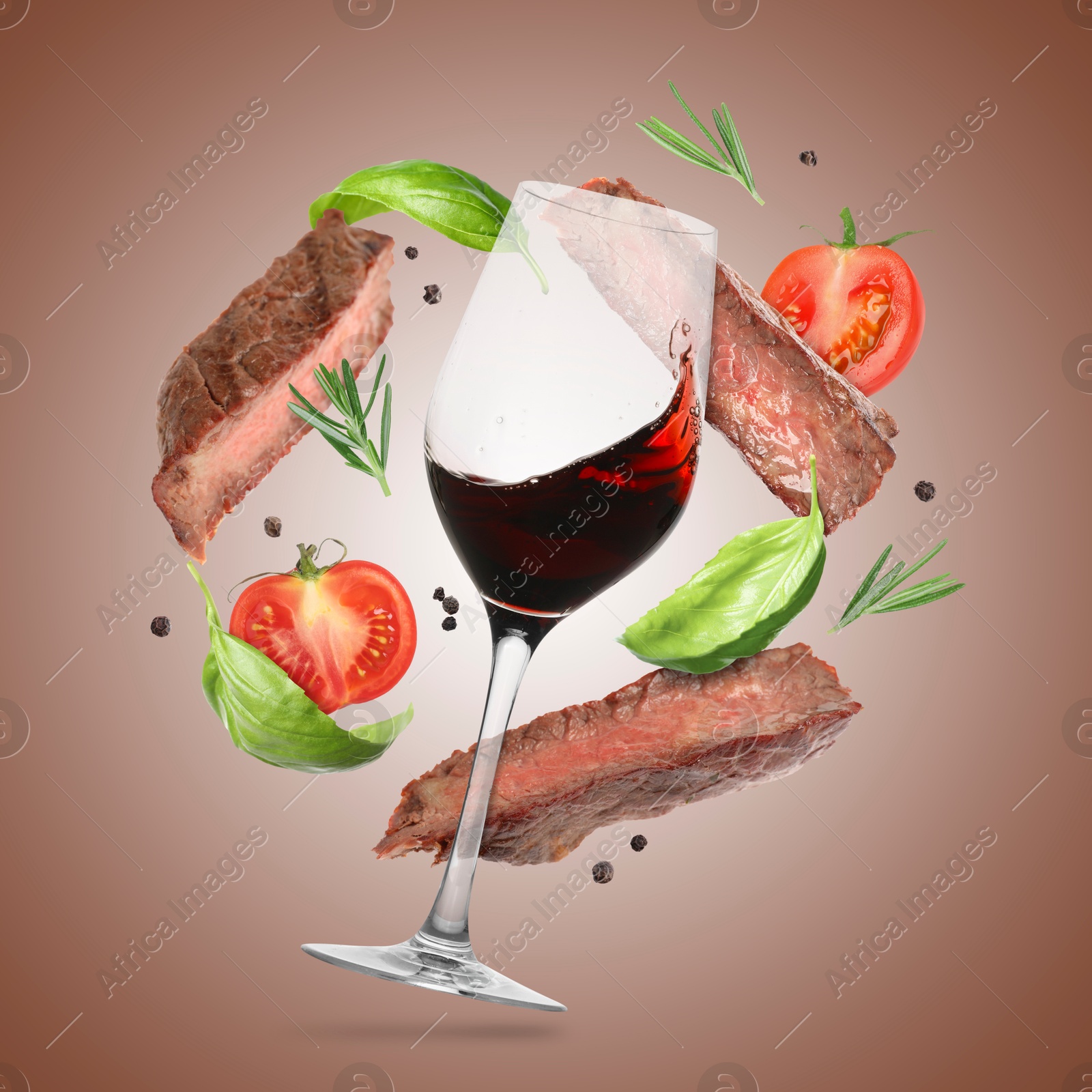 Red wine in glass, grilled beef meat, tomatoes and spices falling on brown gradient background Image of Red wine in glass, grilled beef meat, tomatoes and spices falling on brown gradient background