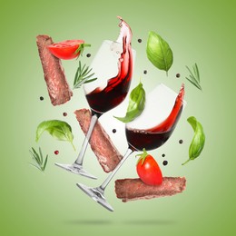 Image of Red wine in glasses, grilled beef meat, tomatoes and spices falling on light green gradient background