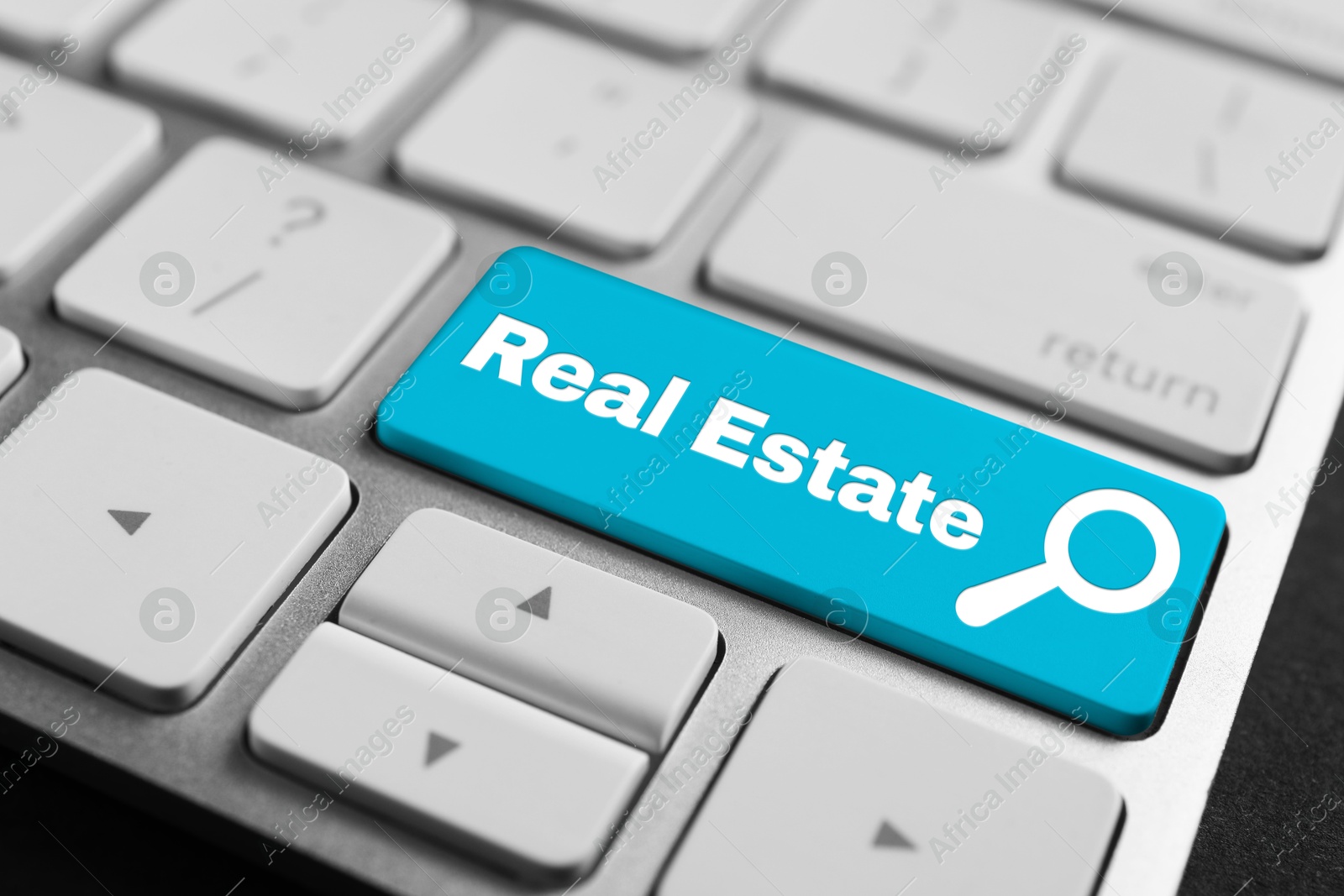 Image of Online accommodation search. Button with magnifying glass icon and words Real Estate on computer keyboard, closeup