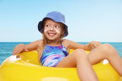 Image of Cute little girl with sunscreen on her skin and inflatable ring in sea. Sun protection while outdoor recreation in summer