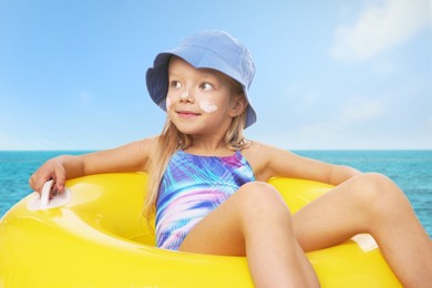 Image of Cute little girl with sunscreen on her skin and inflatable ring in sea. Sun protection while outdoor recreation in summer