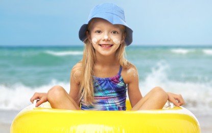 Image of Cute little girl with sunscreen on her skin and inflatable ring in sea. Sun protection while outdoor recreation in summer