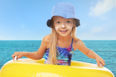 Image of Cute little girl with sunscreen on her skin and inflatable ring in sea. Sun protection while outdoor recreation in summer