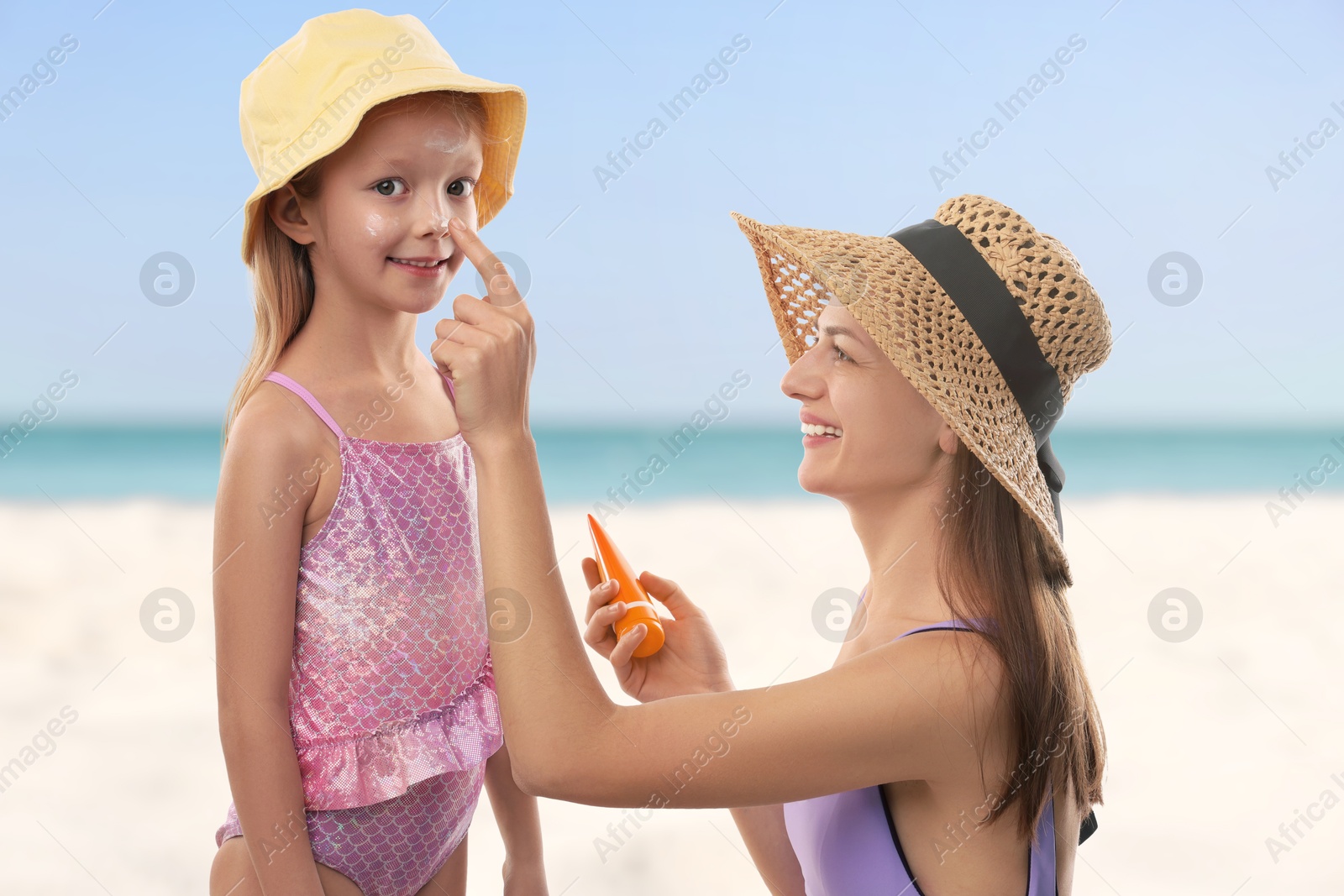 Mother applying sunscreen onto her daughter's face at beach. Sun protection while outdoor recreation in summer Image of Mother applying sunscreen onto her daughter's face at beach. Sun protection while outdoor recreation in summer