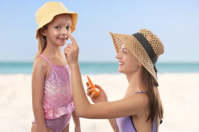 Image of Mother applying sunscreen onto her daughter's face at beach. Sun protection while outdoor recreation in summer