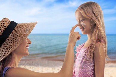 Image of Mother applying sunscreen onto her daughter's face at beach. Sun protection while outdoor recreation in summer