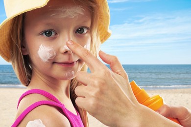 Image of Mother applying sunscreen onto her daughter's face at beach, closeup. Sun protection while outdoor recreation in summer