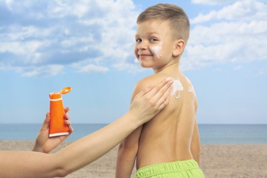 Image of Mother applying sunscreen onto her son's skin at beach, closeup. Sun protection while outdoor recreation in summer