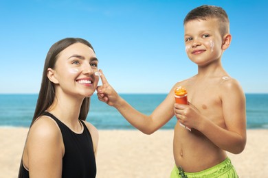 Image of Little boy applying sunscreen onto his mother's face at beach. Sun protection while outdoor recreation in summer