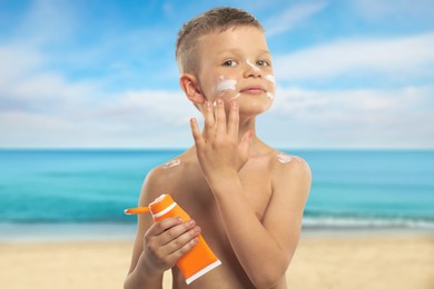 Image of Little boy applying sunscreen on his face at beach. Sun protection while outdoor recreation in summer
