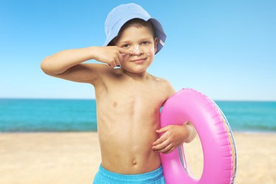 Image of Little boy with sunscreen on his skin holding inflatable ring at beach. Sun protection while outdoor recreation in summer