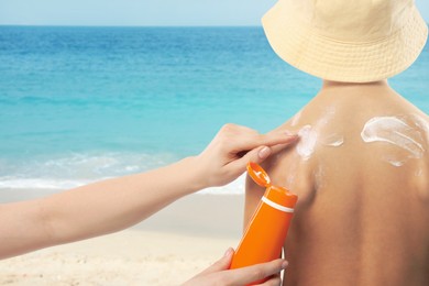 Image of Mother applying sunscreen onto her son's skin at beach, closeup. Sun protection while outdoor recreation in summer
