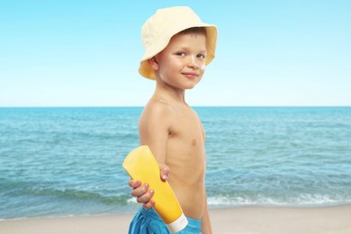 Image of Little boy with tube of sunscreen at beach. Sun protection while outdoor recreation in summer