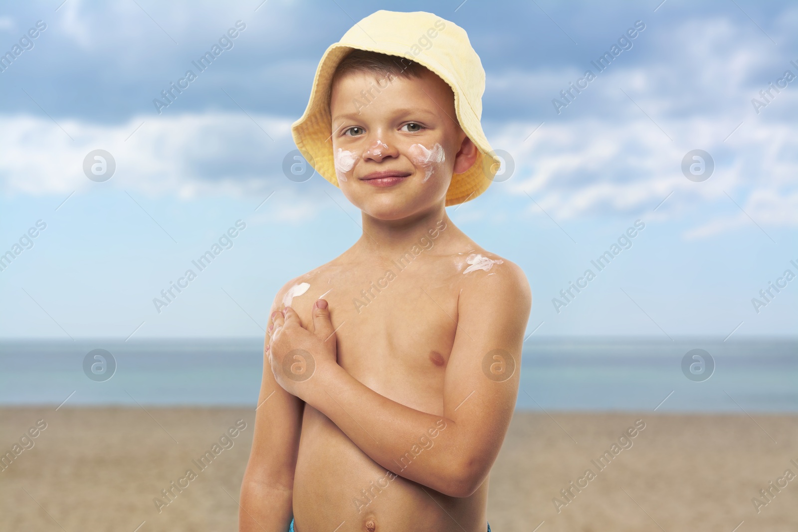Image of Little boy applying sunscreen on his skin at beach. Sun protection while outdoor recreation in summer