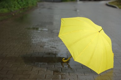 Photo of Yellow umbrella on wet asphalt outdoors, space for text