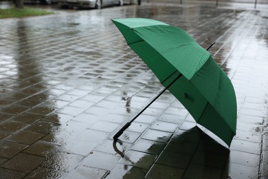 Photo of Green umbrella on wet asphalt outdoors, space for text