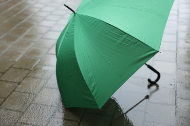Photo of Green umbrella on wet asphalt under heavy rain, closeup. Space for text