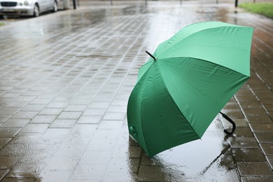 Photo of Green umbrella on wet asphalt under heavy rain, space for text