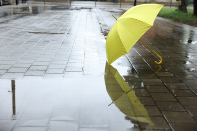 Photo of Yellow umbrella on wet asphalt outdoors, space for text