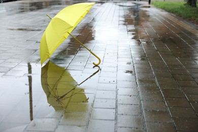 Photo of Yellow umbrella on wet asphalt outdoors, space for text