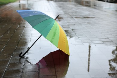 Photo of Colorful umbrella on wet asphalt outdoors, space for text