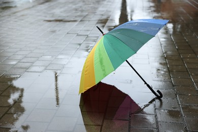 Photo of Colorful umbrella on wet asphalt outdoors, space for text