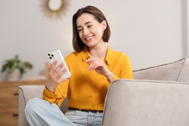 Photo of Woman using modern smartphone in armchair at home
