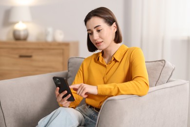 Photo of Woman using modern smartphone in armchair at home