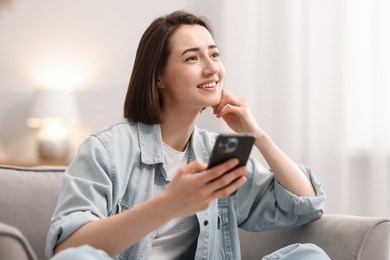 Photo of Woman using modern smartphone in armchair at home