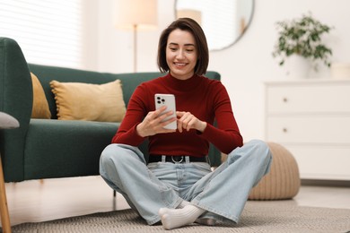 Photo of Woman using modern smartphone on floor at home
