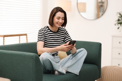Photo of Woman using modern smartphone on sofa at home