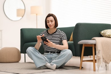 Photo of Woman using modern smartphone on floor at home