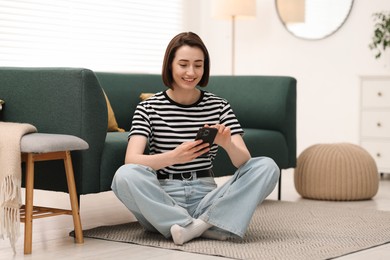 Photo of Woman using modern smartphone on floor at home