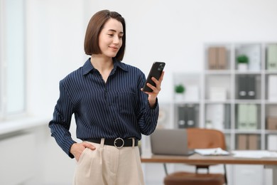 Photo of Beautiful woman using her smartphone in office. Space for text